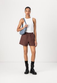 Shorts en lin marron avec une taille élastique, associés à un débardeur blanc et des bottes de combat noires. Un sac bandoulière bleu vient compléter le look.