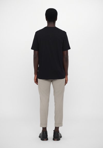 T-shirt noir en coton, à manches courtes, col rond ; associé à un pantalon gris clair retroussé et des chaussures noires avec des accents texturés.