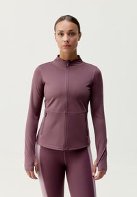 Lilla zip-up sportsjakke med lange ærmer, høj krave og to frontlomme med lynlås. Glat struktur med tætsiddende silhuet.