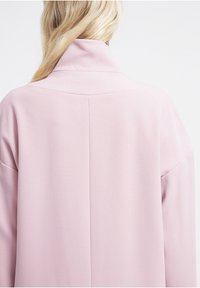 Light pink jacket featuring a high collar, smooth texture, oversized fit, and a seam detail running down the back.