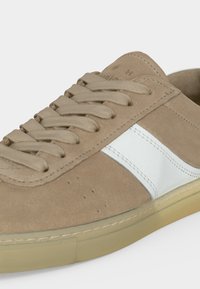 Baskets en daim beige avec bande en cuir blanc, lacets beiges et semelle en caoutchouc beige, vues de côté et légèrement de dessus.