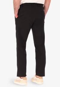 Pantaloni neri con vestibilità su misura, dotati di due tasche posteriori, texture liscia e orlo pulito. Abbinati a sneaker chiare.