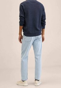 Suéter azul marino con cuello redondo, jeans azul claro de corte recto, zapatillas beige, textura suave y detalles mínimos en la ropa.