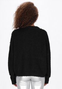 Fekete, túlnagy kötött pulóver, puha textúrával és lecsüngő vállakkal. Hosszú ujjú, bordázott aljánál, fényes ezüst nadrággal párosítva.