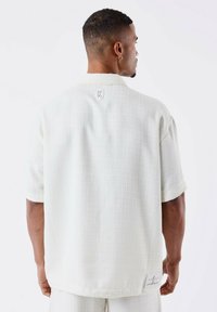 Witte korte mouw shirt van textuurstof, met open kraag en logodetail op de rug. Casual pasvorm met een subtiel geweven patroon.