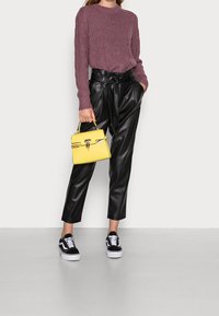 Purple knit sweater, black faux leather trousers with a belted waist, yellow handbag, and black sneakers with white soles.