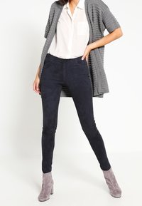 Mörkblå mockabyxors slim fit, i kombination med en ljusgrå öppenstickad kofta och grå ankelboots.