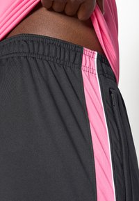 Μαύρο σορτς με ροζ διχτυωτό ένθετο και λευκή ρίγα. Ελαστική μέση και λεπτομέρεια με τσέπη στο πλάι. Λείος υφασμάτινος τύπος, αθλητικός σχεδιασμός.