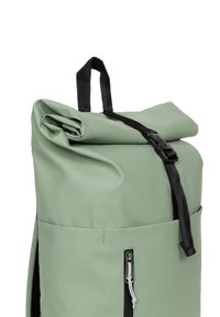 Zaino roll-top verde menta con spallacci neri, dotato di tasca frontale con zip e materiale testurizzato. Design compatto e moderno.