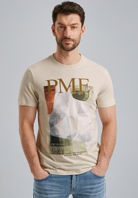 Béžové bavlněné tričko s grafickým potiskem různobarevných tvarů a textu. Krátké rukávy a design s kulatým výstřihem.