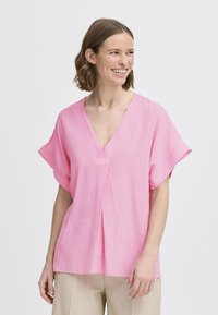 Rosa kortærmet top med v-hals, tekstureret stof, løs pasform og central plissé detalje, parret med lyse beige bukser.