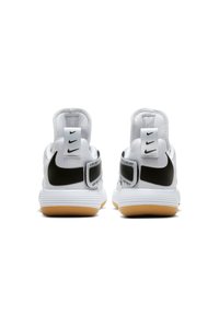 Baskets de sport blanches avec des accents noirs et un tissu texturé. Elles présentent une semelle en caoutchouc gomme et une marque "Just Do It" sur les sangles du talon.
