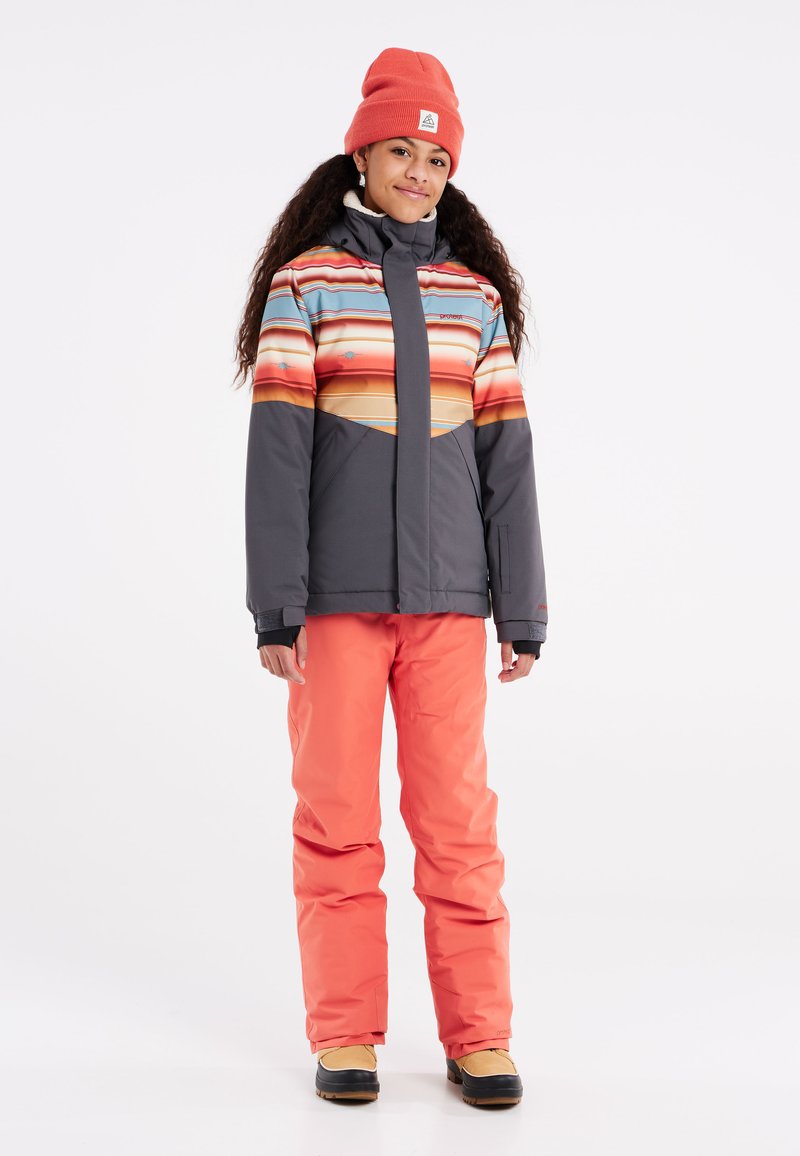Skijack met meerkleurige horizontale strepen in tinten oranje, grijze broek en zwarte laarzen; warme stof, ritsluiting en capuchon.