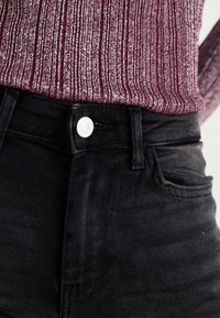 Black denim jeans featuring a high waist, five-pocket design, and metal button closure. The fabric has a smooth texture with minimal fading.