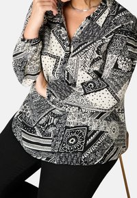 Blusa a fantasia in bianco e nero con vari disegni geometrici e motivi floreali, con colletto con bottoni e maniche elasticizzate.