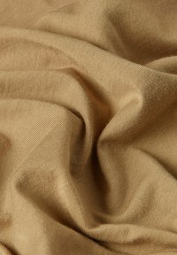 Tessuto marrone chiaro con una superficie morbida e testurizzata, caratterizzato da pieghe e ondulazioni delicate, che indicano un materiale leggero e flessibile.