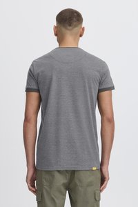 Grå kortærmet T-shirt med rund halsudskæring og kontrastfarvede mørkegrønne manchetter, parret med olivengrønne cargo-bukser. Lille logo-detalje ved kanten.