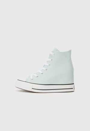 Højtop lys grøn lærredsneaker med hvide snørebånd og gummisål, set fra den indvendige side mod en ensfarvet baggrund.