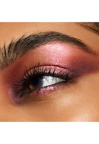 Gros plan sur un œil avec un fard à paupières rose et violet pailleté, des cils noirs bien définis et un éclat réfléchissant sur la cornée.