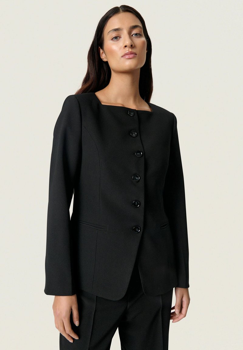 Mustast kohandatud bleiser ruudukujulise kaelusega, kuus musta nööpi, pikad varrukad ja struktureeritud siluett. Sile kangas peene tekstuuriga.