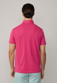 Polo tričko s krátkým rukávem v jasně růžové barvě, s klasickým límečkem a hladkým, lehkým materiálem. Žádné viditelné vzory ani akcenty.