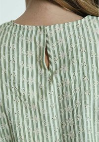 Grön- och vitrandig tyg med blommiga broderidetaljer och en liten öppning bak. Mjuk textur med en lätt känsla.