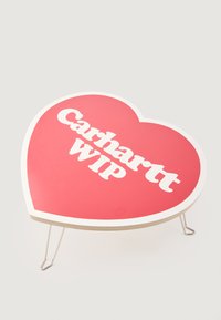 Stôl v tvare srdca s lesklým červeným povrchom, bielym textom 'Carhartt WIP' a kovovými nohami pre oporu. Okrúhly dizajn s hladkými hranami.