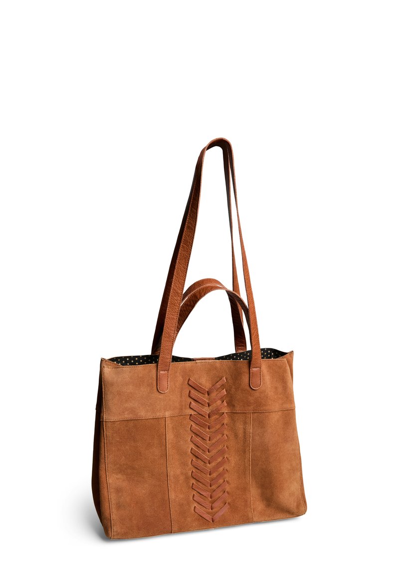 Sac fourre-tout en suède marron avec deux poignées, présentant un design décoratif en laçage sur le devant et une doublure à pois à l'intérieur.