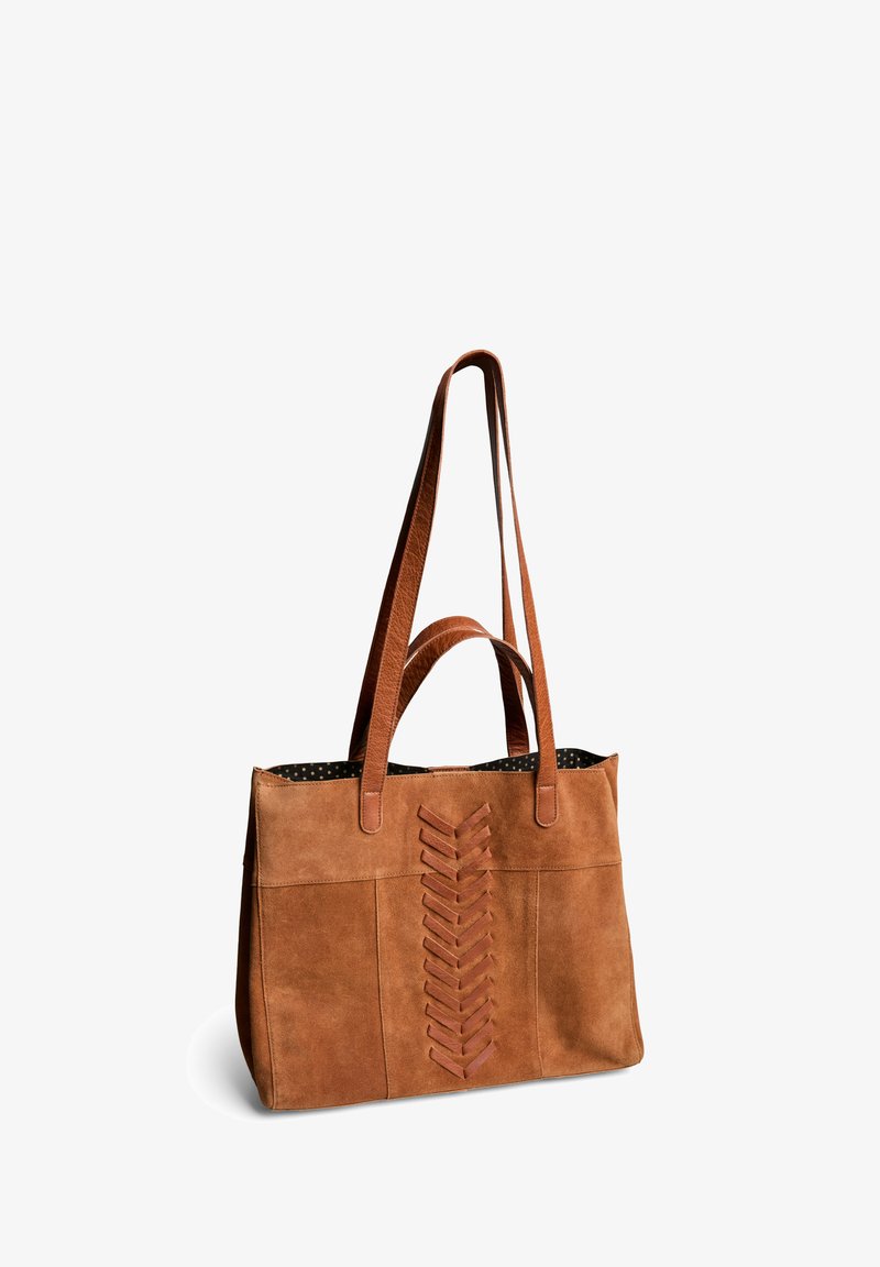 Sac fourre-tout en suède marron avec deux poignées, présentant un design décoratif en laçage sur le devant et une doublure à pois à l'intérieur.