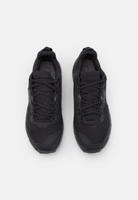 Czarne buty sportowe z teksturowanej siateczki, wzmocnionym czubkiem oraz płaskimi sznurowadłami. Oferują lekką konstrukcję i minimalne oznakowanie po boku.