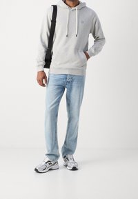 Sudadera gris con capucha y cordones, bolsillo frontal; jeans rectos de mezclilla azul claro; zapatillas gris y blancas con acentos negros.