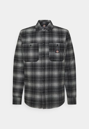 Camicia di flanella a quadri bianca e nera con maniche lunghe, chiusura frontale con bottoni, due tasche sul petto e una toppa con logo sopra la tasca sinistra.