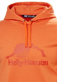 Sudadera naranja con capucha ajustable, textura suave y un diseño gráfico de montañas y un sol, con el logo de "Helly-Hansen" debajo.