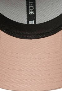 Soft pink fabric cap with a black brim and inner lining. Features 9FORTY branding and textured surface. Rounded shape for a snug fit.