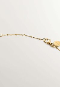 Pulsera de cadena de oro con un cierre de langosta, eslabones circulares y un charm redondo con detalles grabados. Textura suave con acabado pulido.
