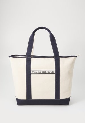 Canvas-Tragetasche in Creme mit dunkelblauen Griffen und Besatz, mit dem mittig vorne aufgestickten "Tommy Hilfiger" Logo.