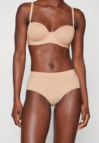 Nude beige undergarment set featuring a padded bra with adjustable straps and high-waisted briefs, made from smooth, stretchy material.