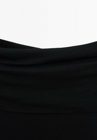 Gros plan d'un tissu noir plié deux fois horizontalement sur fond blanc, montrant une texture douce et un léger drapé.