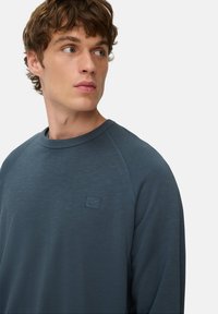 Niebieski sweatshirt z okrągłym dekoltem, rękawami raglanowymi i teksturowanym wykończeniem. Posiada małe logo na piersi w pasującym odcieniu.