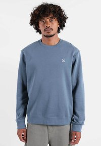 Sweat-shirt bleu à col ras du cou en tissu lisse, avec un petit logo flocon de neige brodé sur la poitrine et des poignets et ourlet côtelés.