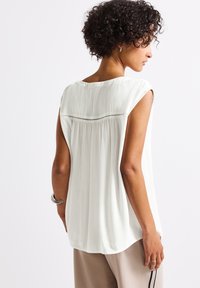 White, lightweight sleeveless top with a textured finish, rounded neckline, and subtle detailing across the back.
