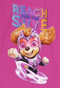 Rosa T-Shirts mit einem Cartoon-Charakter mit braunem Fell, der ein lila Superhelden-Outfit und eine Schutzbrille trägt und eine Pfote nach vorne ausstreckt.