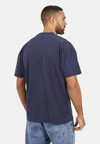 T-shirt en coton bleu marine à manches courtes, col rond, coupe décontractée, sans motifs ni accents visibles, associé à un jean en denim clair.