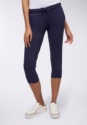 Jogging in blu navy accorciati realizzati in materiale morbido con vita regolabile e risvolti, abbinati a sneakers bianche con accenti dorati.