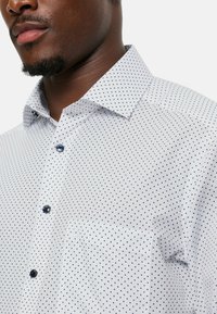 Witte button-up shirt met marineblauwe stippen. Heeft een klassieke kraag en een borstzak. Blauwe knopen passen goed bij het ontwerp.