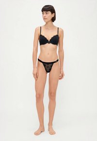 Černá krajková podprsenka s kosticemi a nastavitelnými ramínky, doplněná o odpovídající černé průsvitné tanga s květinovým vzorem.