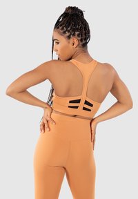 Sportbh i ljusorange med racerback-design, med svarta accentränder och en slät textur. Matchas med högmidjade leggings i samma färg.