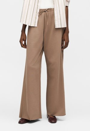 Pruunid laia lõikega püksid nööriga vöökoht, kantud tumedate pruunide kingade ja valge triibulise särgiga valge topi peal.