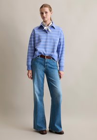 Lichtblauwe gestreepte sweatshirt met een kraag, gecombineerd met wijde, vervaagde blauwe jeans en een bruine riem. Afgemaakt met enkellaarsjes.