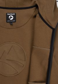 Bruine jas met zwarte afwerking, voorzien van een reliëf berglogo en een label "Travelin' where we walk" maat large in de kraag.